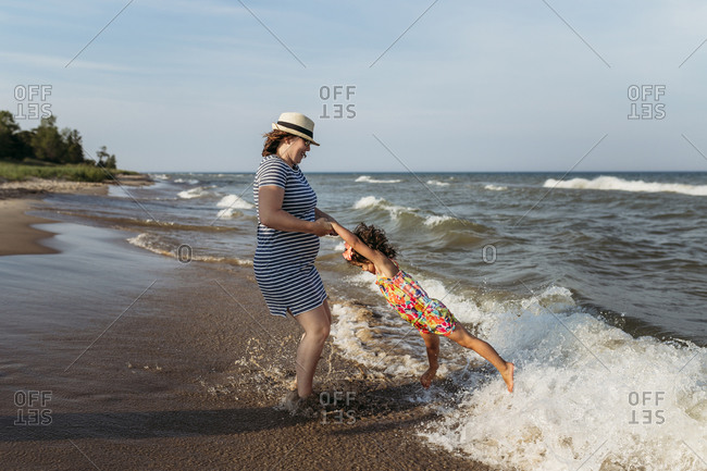 Playful mother spinning daughter at beach against sky