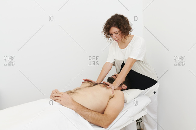 Physiotherapist treating the chest and shoulders of a male patient lying on an examination table in her office