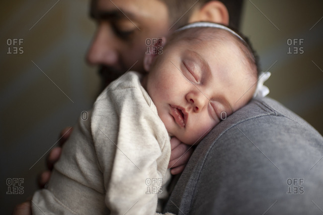 Close up of newborn baby's face sleeping on father's shoulder at home