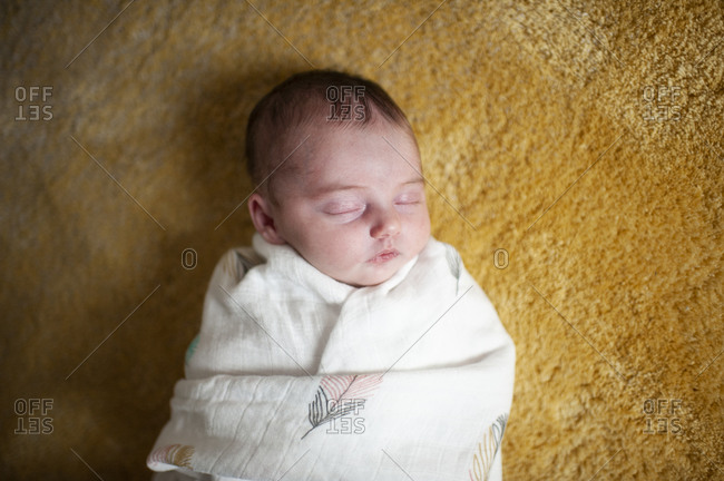Newborn baby girl wrapped up in blanket sleeping at home on yellow rug