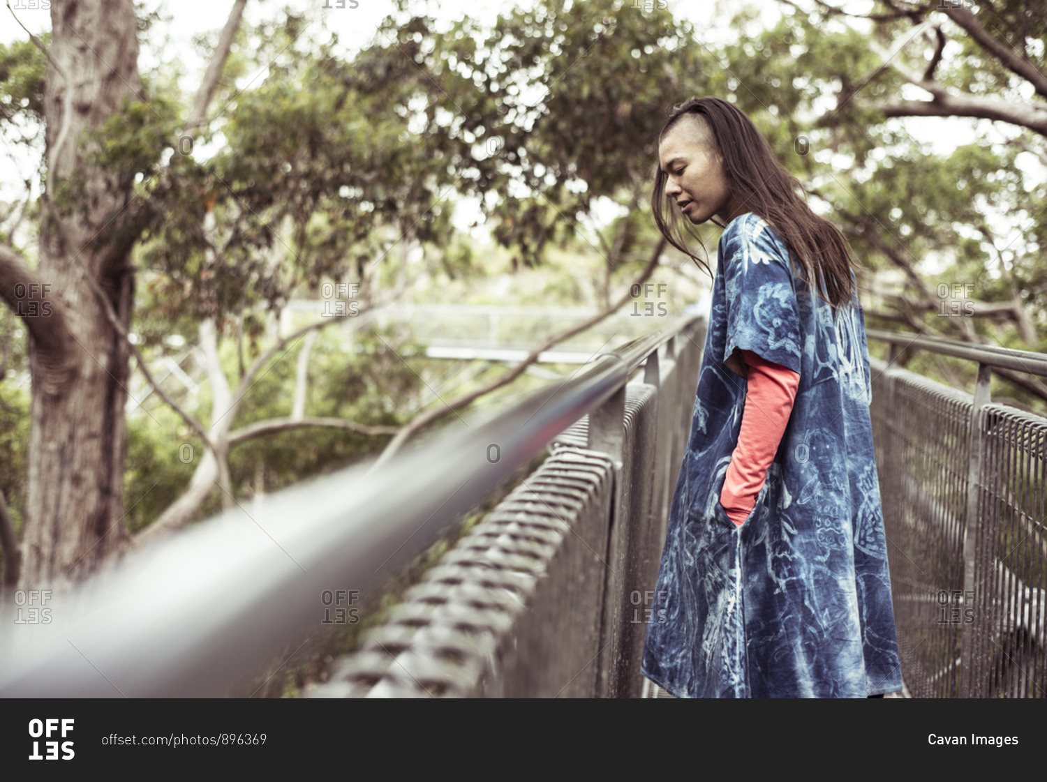 mixed race androgynous woman with blue dress looks out on tree top walk