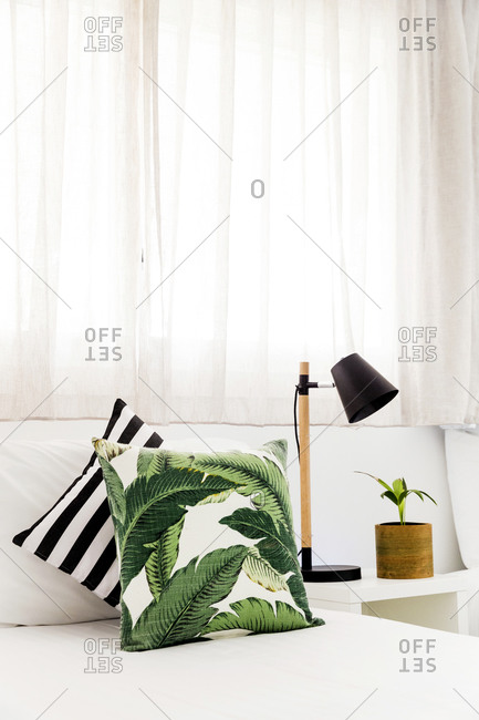 Pillows on a wooden bench beside plant and lamp