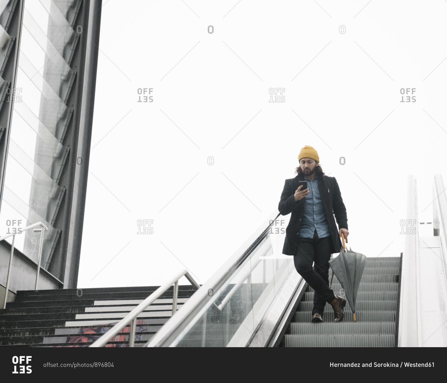 Man with umbrella standing on  escalator looking at smartphone- Berlin- Germany