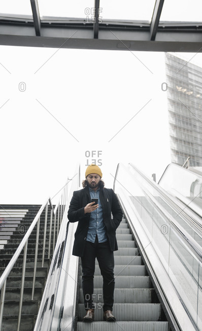 Man standing on escalator looking at smartphone- Berlin- Germany