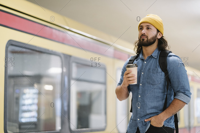 Portrait of man with backpack and coffee to go waiting at platform- Berlin- Germany