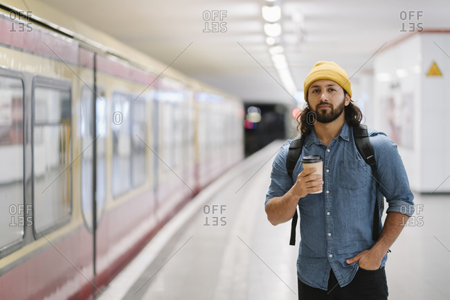 Portrait of man with backpack and coffee to go waiting at platform- Berlin- Germany