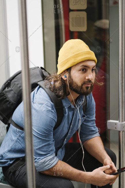 Man with backpack listening music with smartphone and earphones in commuter line- Berlin- Germany