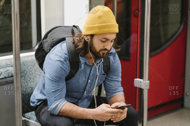 Man with backpack listening music with smartphone and earphones in commuter line- Berlin- Germany