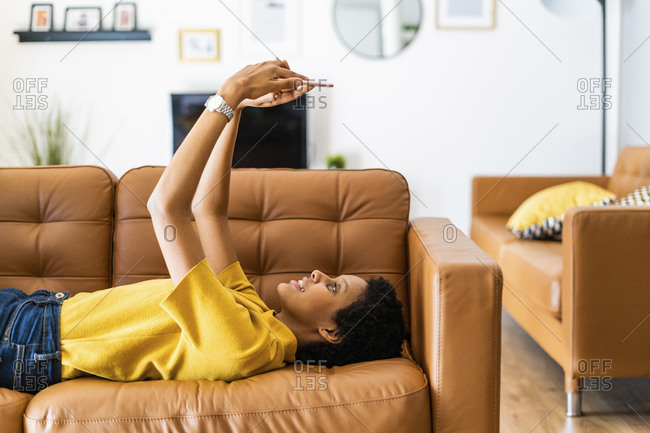 Young woman lying on couch at home using smartphone