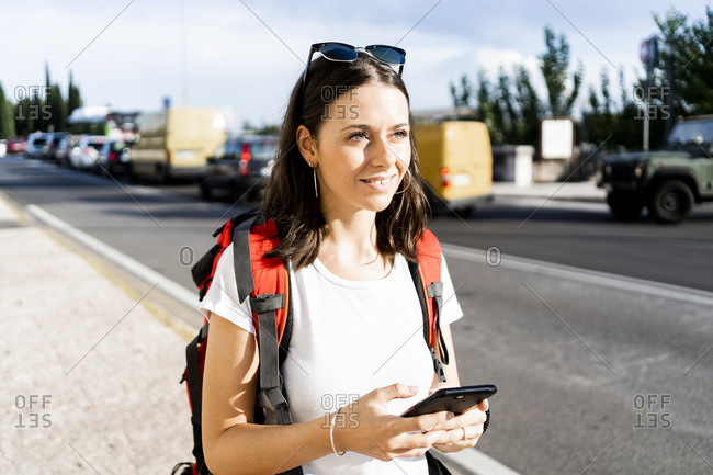 Young female backpacker with red backpack using smartphone in the city- Verona- Italy