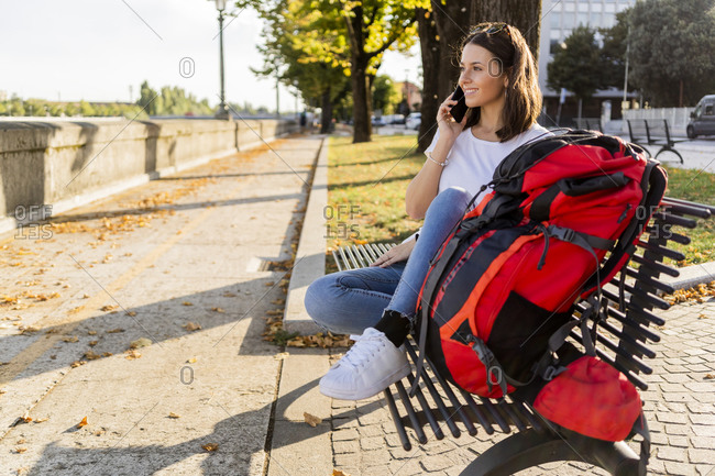 Young female backpacker with red backpack using smartphone- sitting on a benach in Verona- Italy