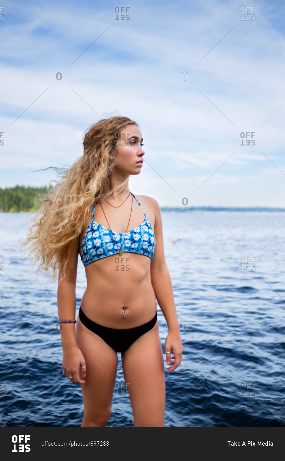 Young blonde woman in a blue bikini standing lakeside stock photo - OFFSET