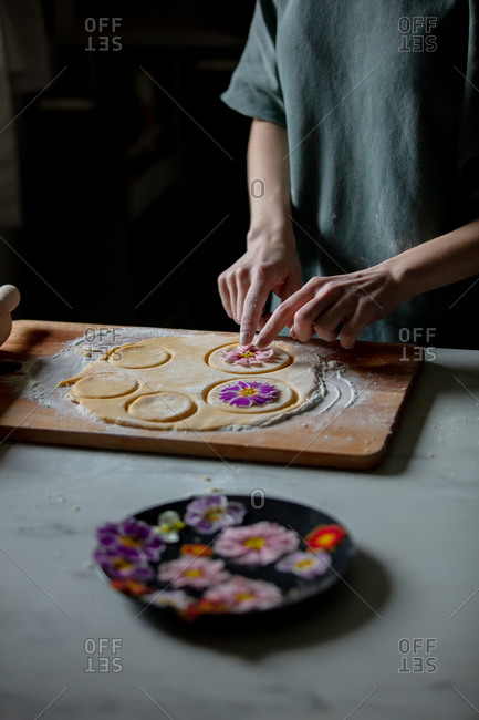 Woman making cookies with primula petals at kitchen table.