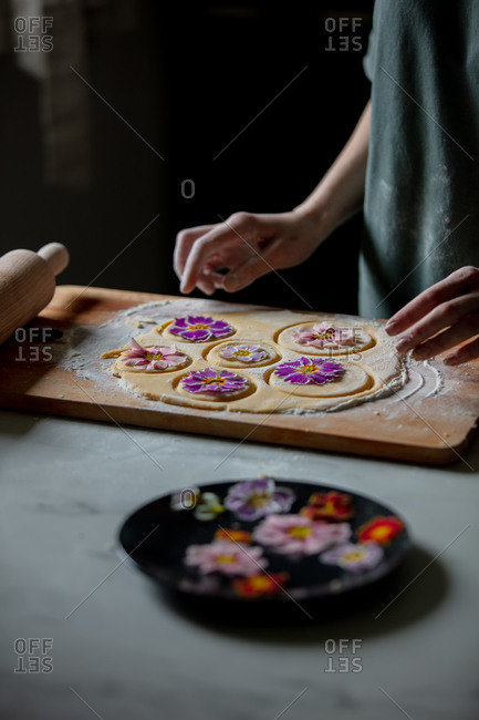 Woman making cookies with primula petals at kitchen table.