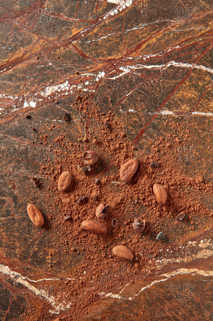 Freshly roasted natural organic beans and crushed cocoa powder on a brown granite stone background