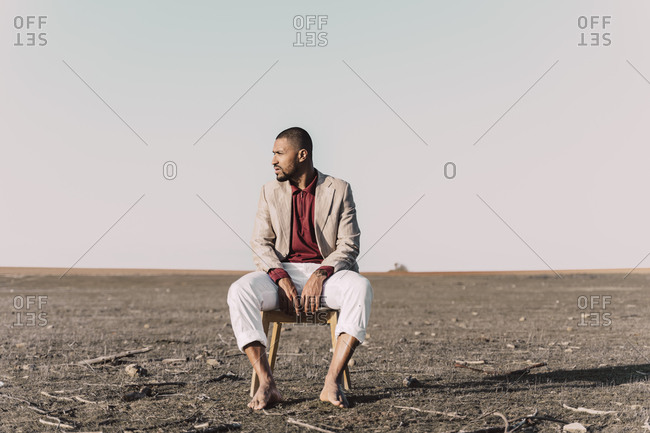 Young man sitting on chair in barren land