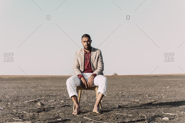 Portrait of young man sitting on chair in barren land