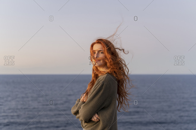 Portrait of redheaded young woman with windswept hair at the coast at sunset- Ibiza- Spain
