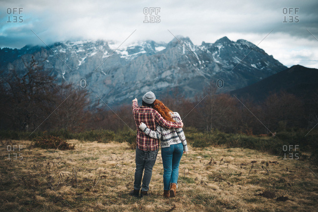 Back view of tender couple hugging and bonding in cold day in mountains