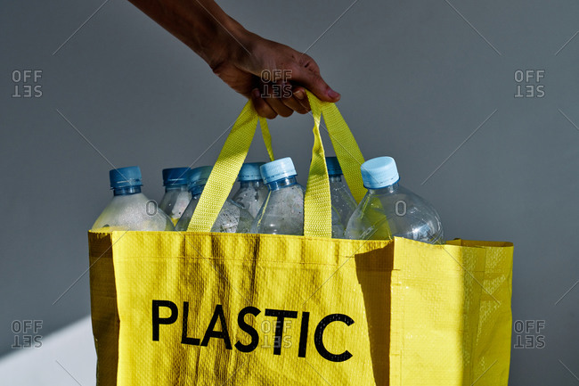 Unrecognizable person carrying yellow bag full of plastic empty water bottles on gray background in studio
