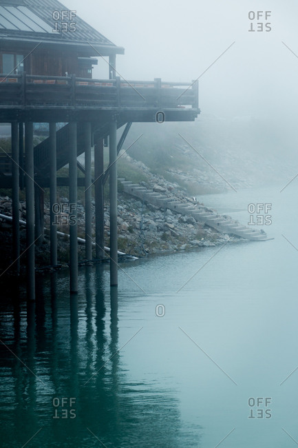 Mysterious timber house raised on piles over lake surface in misty weather in Austria