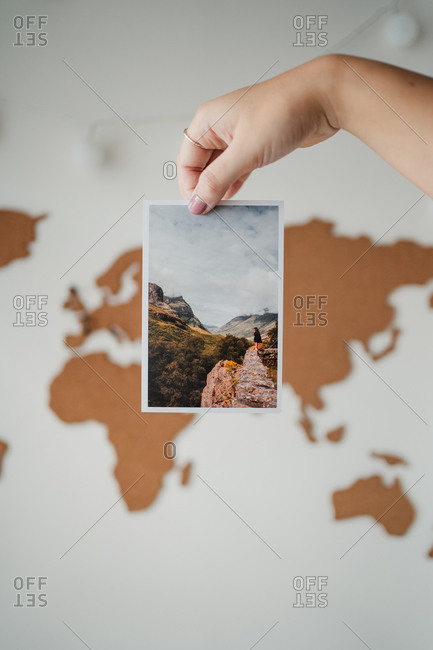 Crop unrecognizable female holding postcard in front of wall world map at home in Paris