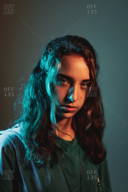 Focused youthful long haired Hispanic female model in casual clothes looking at camera in studio on gray background