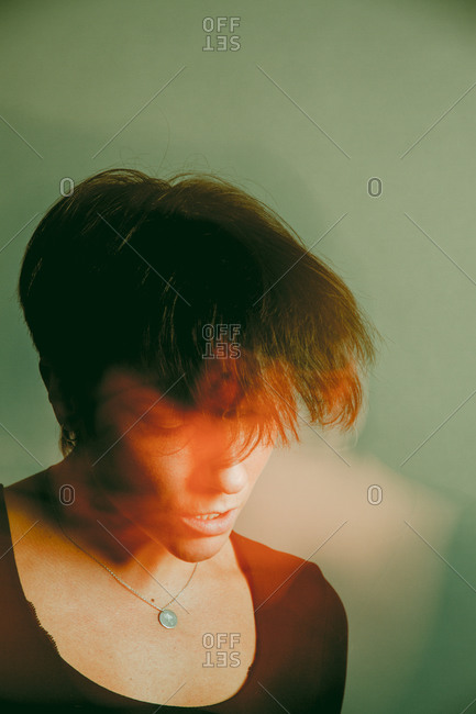 Long exposure of pensive youthful female with short hair and in black clothes looking down in studio on olive green background
