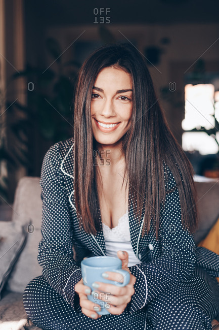 Portrait of beautiful happy young woman drinking morning coffee at her home. Posing for the camera and smiling