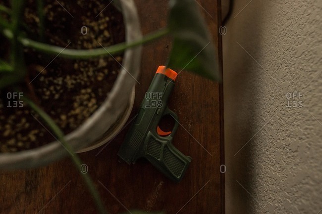 Green and orange toy gun on floor behind plant