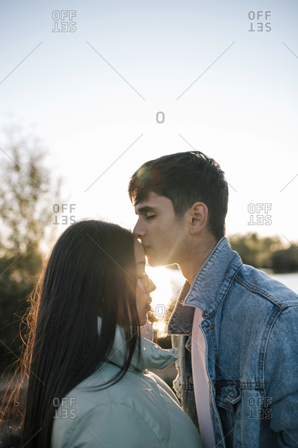 Teenage boy kissing his girlfriend at backlight