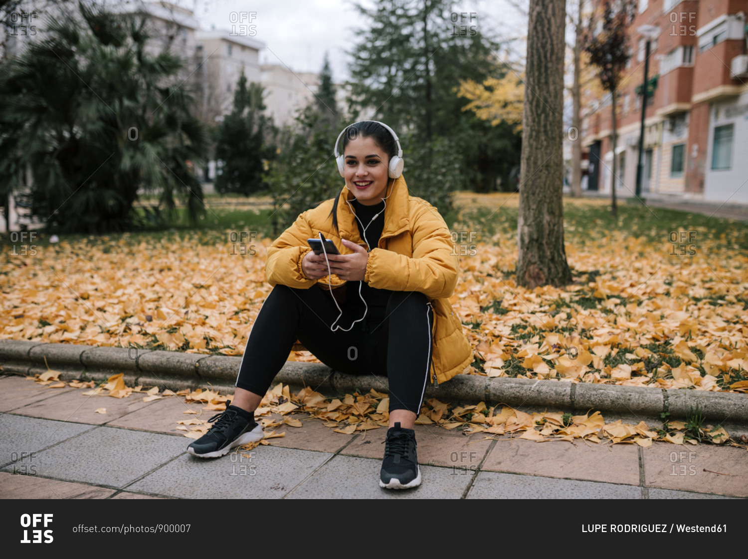 Portrait of smiling young woman  listening music with headphones and smartphone in autumn