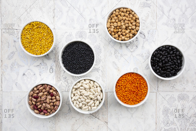 Various legumes in bowls: chickpeas- cannellini beans- quail beans- black beans- yellow lentils- red lentils- black lentils