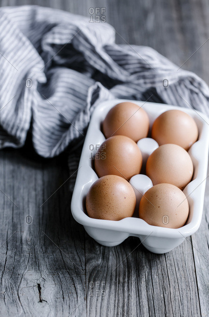 Six eggs in a ceramic egg dish with a napkin.