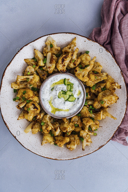 Roasted spicy cauliflower wings in a ceramic bowl served with a small bowl of yogurt cucumber dip