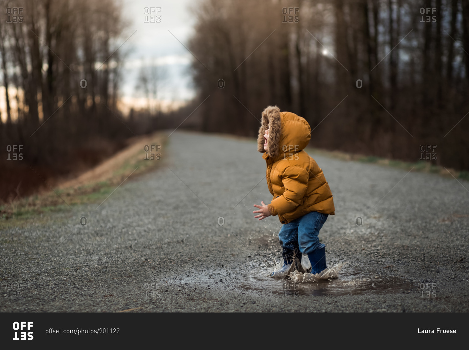 Toddler boy jumping in a puddle with a stick on a rural path