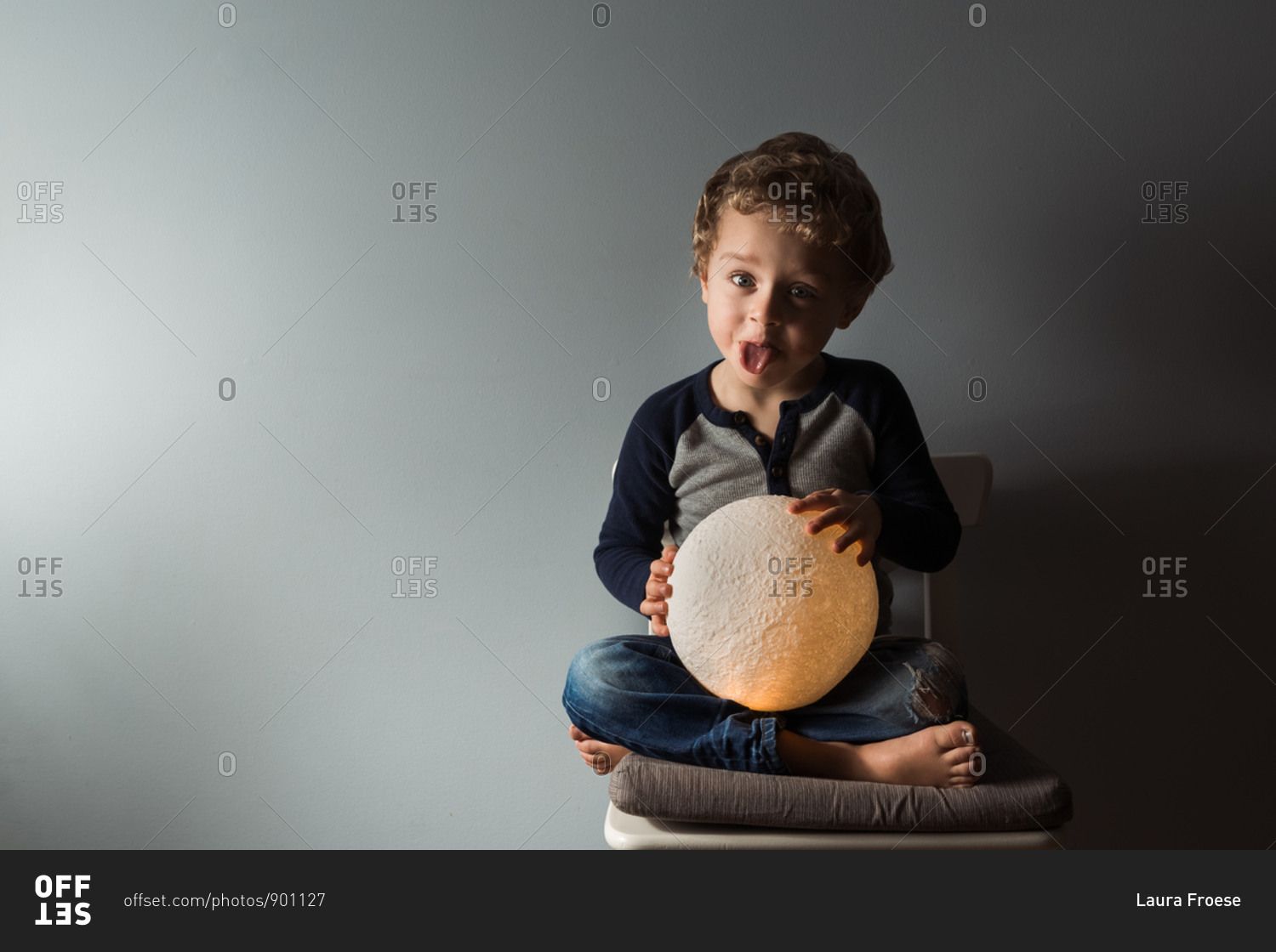 Young boy sticking tongue out while holding round moon lamp