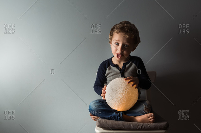Young boy sticking tongue out while holding round moon lamp