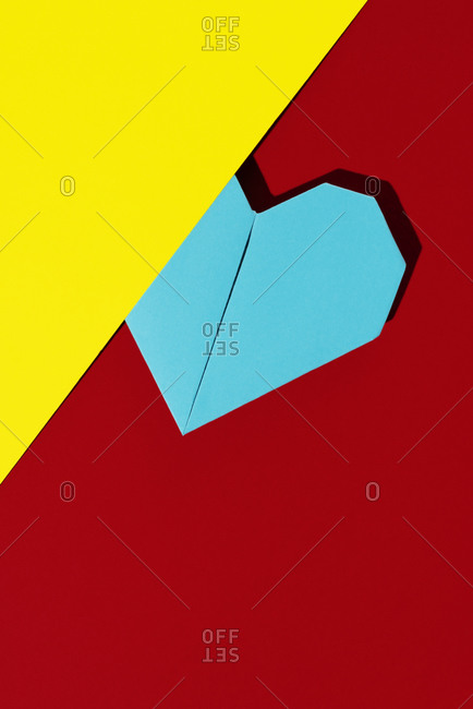 Blue origami heart on a red and yellow paper background