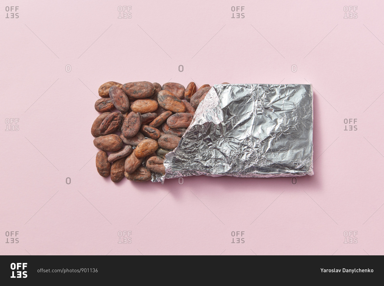 Natural cocoa beans as a chocolate bar in tin foil on a light pink background with copy space.