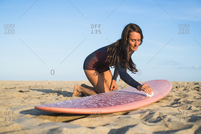 Water woman waxing her new surfboard in preparation for sunset surf