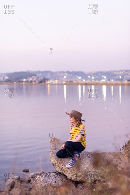 Tween with wide brimmed hat looks out over bay at twilight