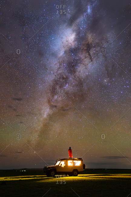 Man on top of a safari truck with milky way in the background