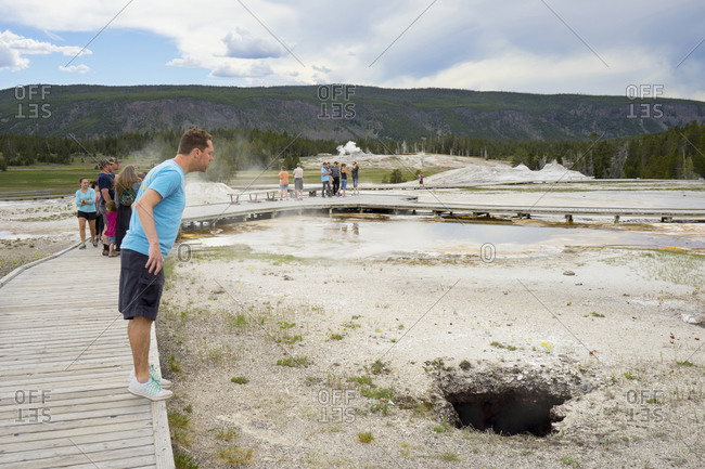 United States, Wyoming, Yellowstone National Park - June 5, 2016: Man looks down a volcanic spring dark hole at the upper geyser basin