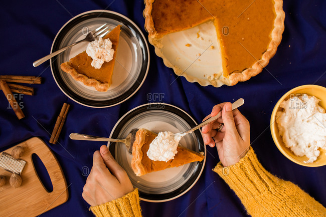 Top view of a woman serving a piece of pumpkin pie with whipped cream