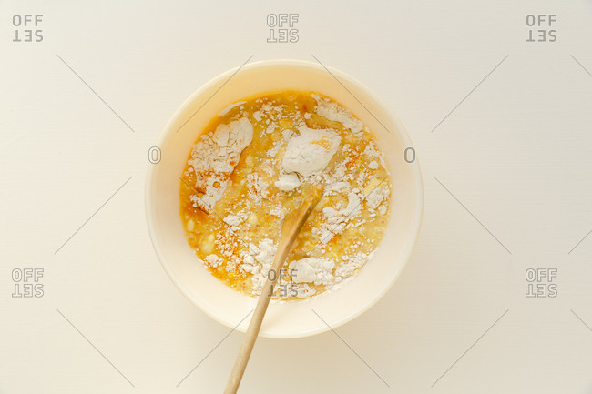 Mix of cake batter in a bowl with wooden spoon on white surface
