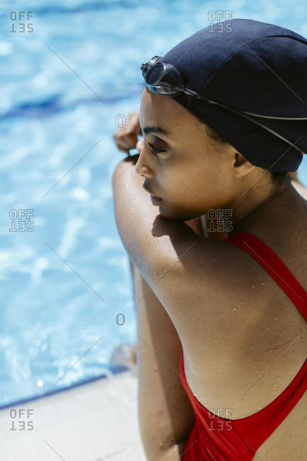 Young woman with swimming cap and  goggles relaxing at poolside after swimming