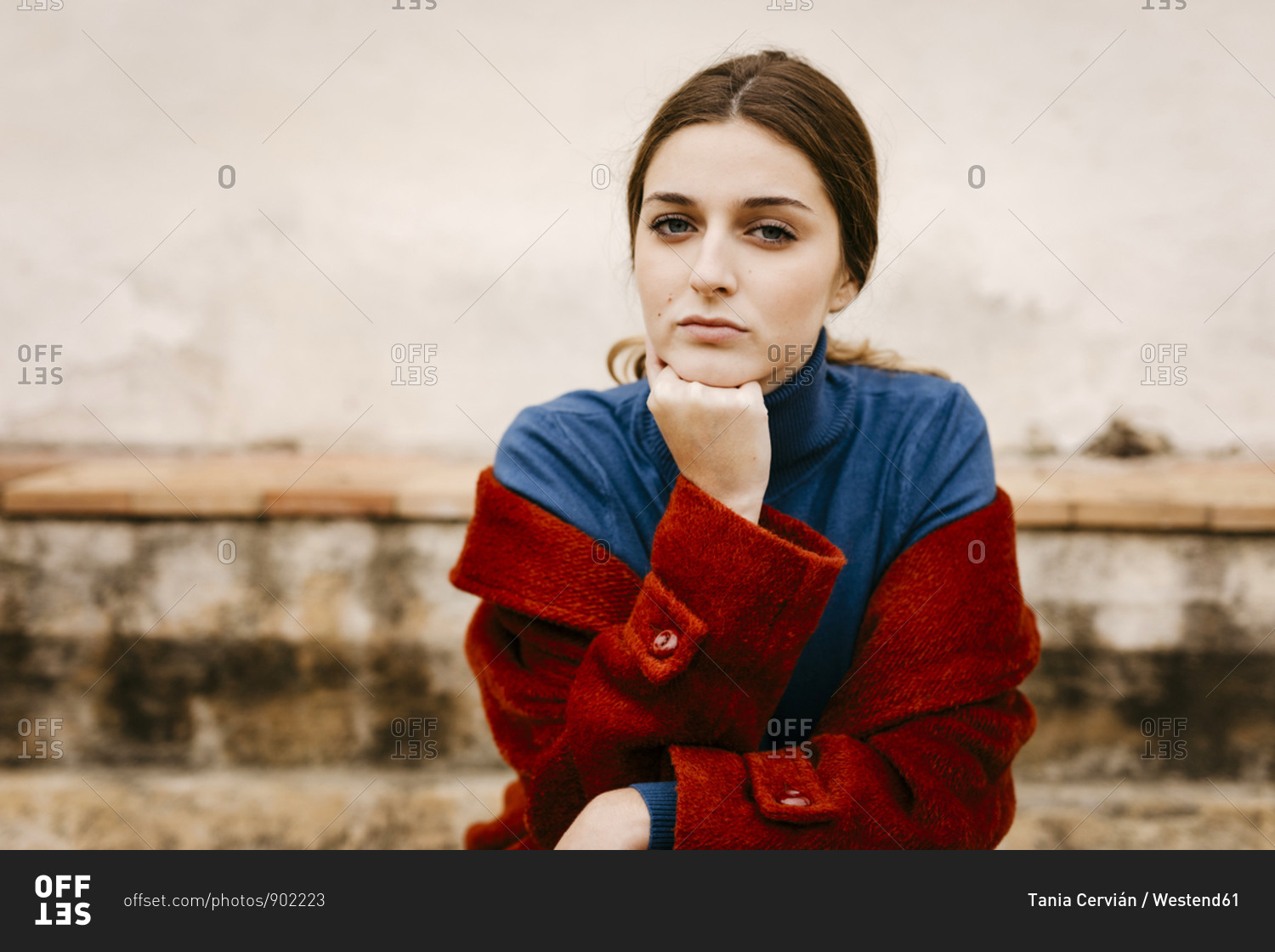 Close up portrait of woman with blue turtleneck pullover and red coat- hand on chin
