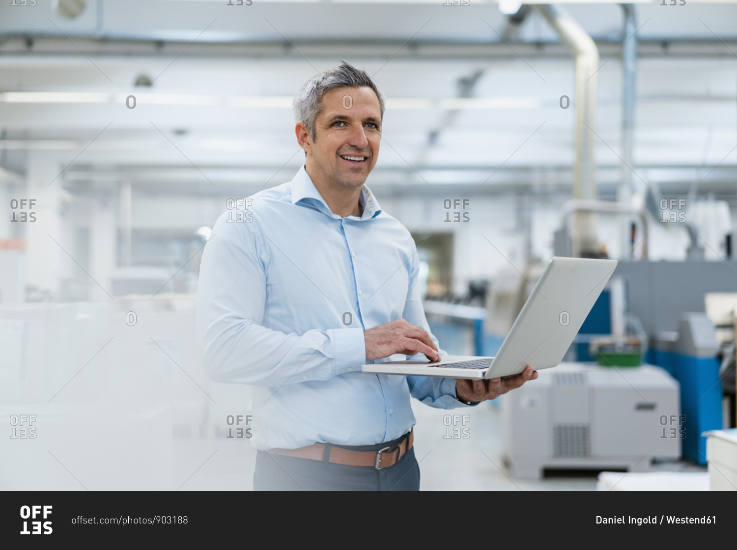 Smiling businessman using laptop in factory