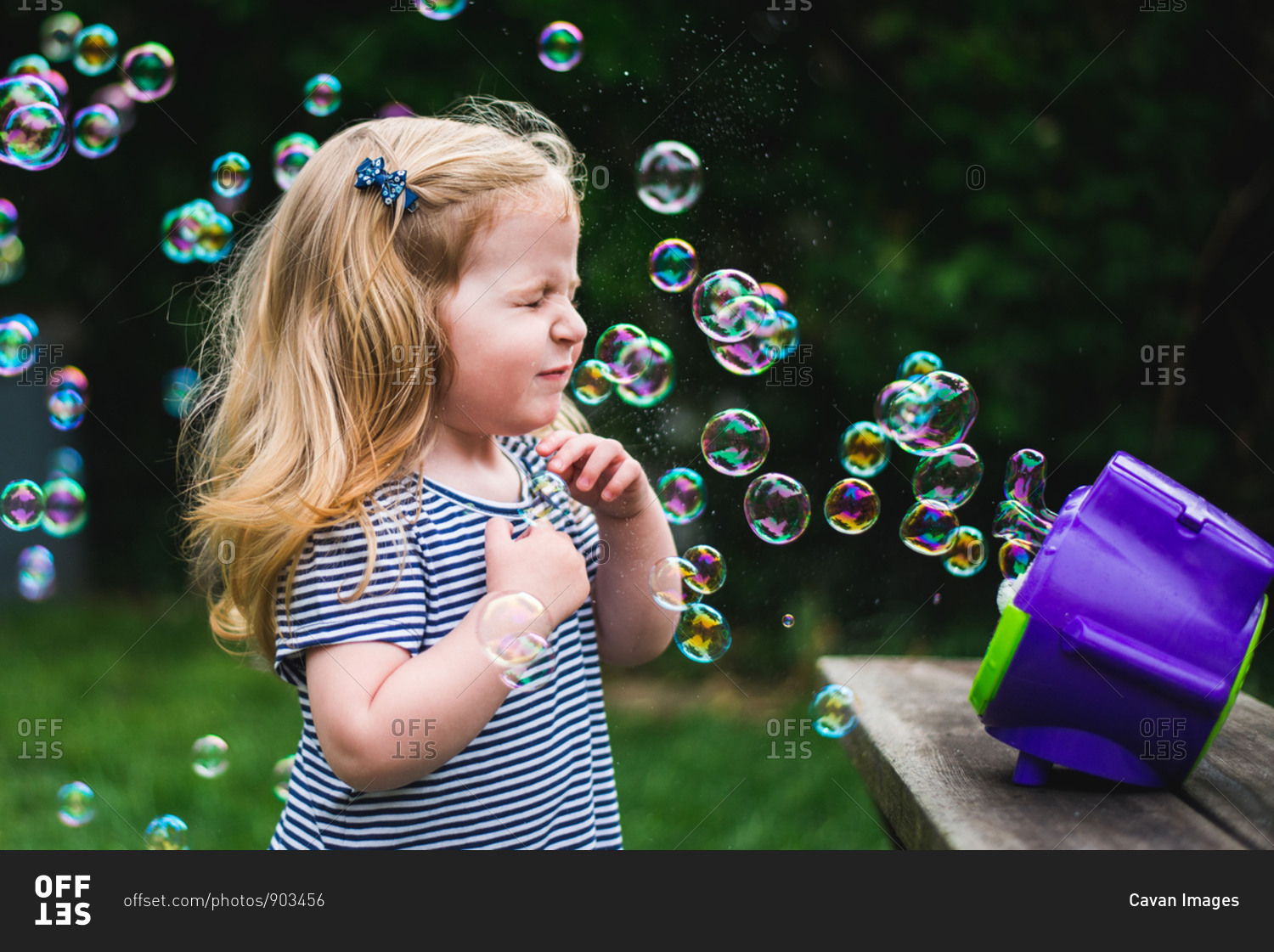 A little girl stands in front of a bubble machine.